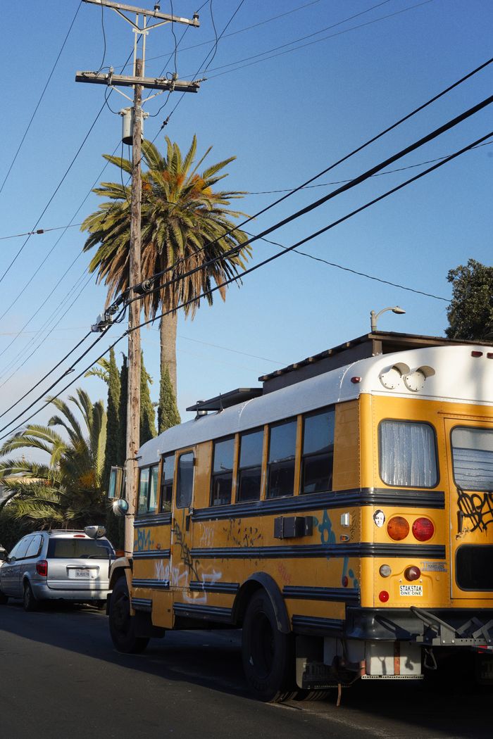 A vandalized school bus parked on a street in Los Angeles with palm trees in the background.