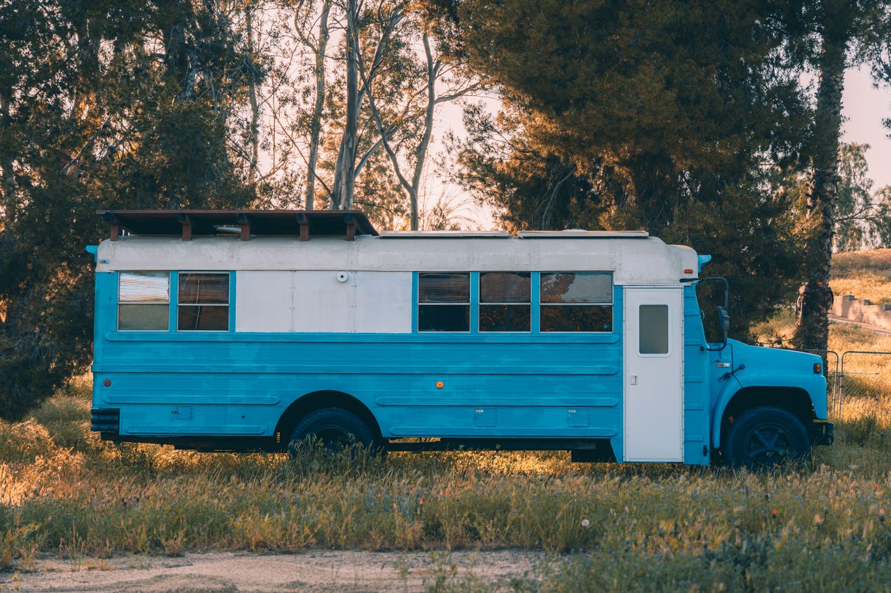 A retro blue school bus parked amidst lush trees in Temecula, California under a warm autumn sunset.