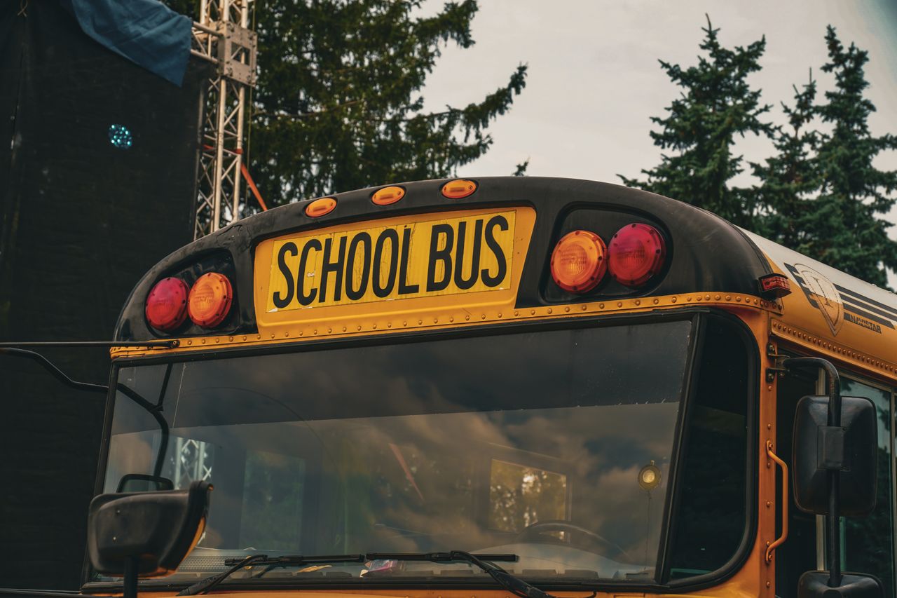 Yellow school bus outdoors in Kyiv, Ukraine, with trees and metal structures in background.
