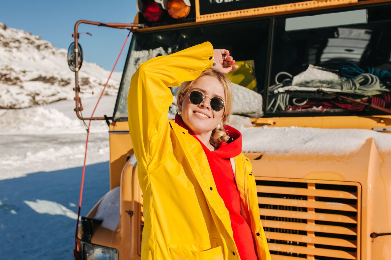 Woman in bright jacket smiling, posing by a snow-covered school bus