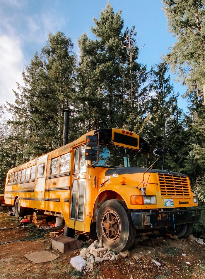 A vintage yellow school bus sits abandoned in a dense forest, evocative of nostalgia and adventure.